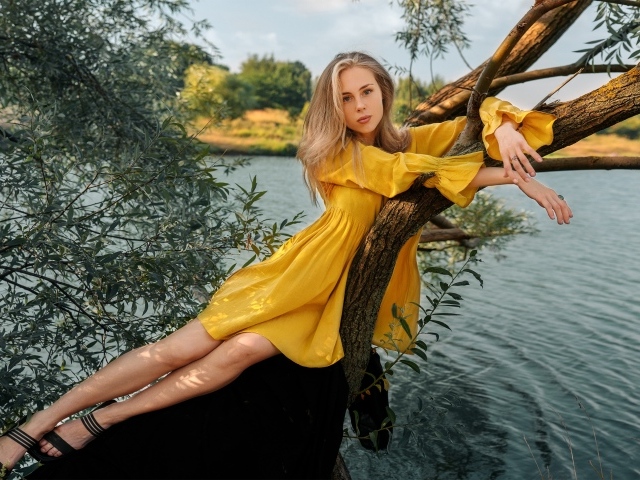Красивая девушка в желтом платье лежит на дереве у воды
