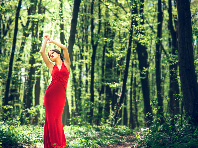 Девушка в красивом красном платье стоит в лесу