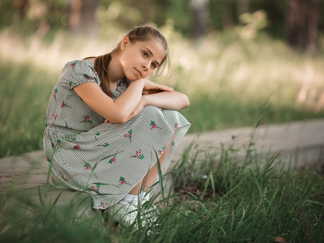 Девушка в платье сидит у зеленой травы