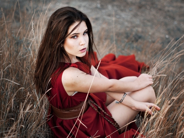 Девушка в красном платье сидит в траве