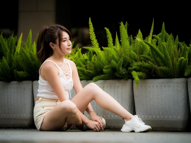 Девушка азиатка сидит на земле у зеленых растений