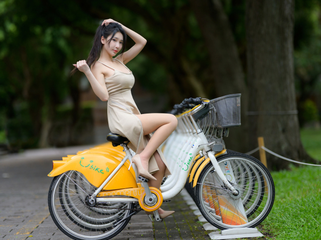 Азиатка в платье сидит на велосипеде