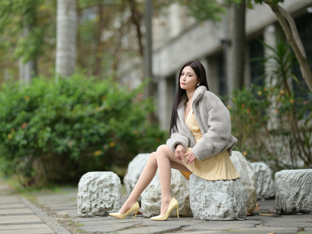 Азиатка в шубе сидит на квадратном камне