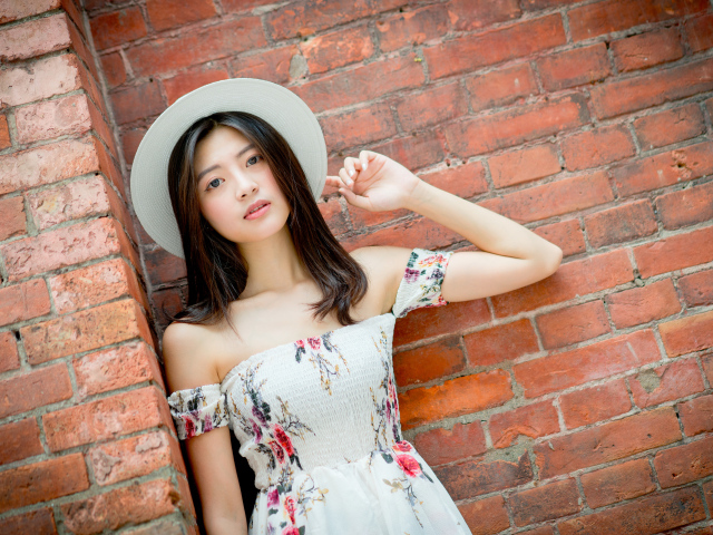 Азиатка в белой шляпе стоит у кирпичной стены