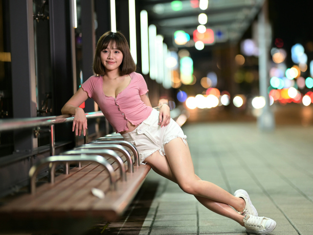 Азиатка в коротких белых шортах сидит на остановке