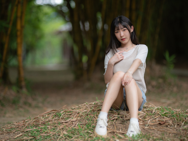 Азиатка сидит на земле в парке