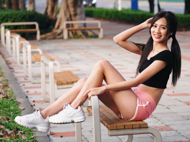 Спортивная девушка азиатка сидит на лавке 