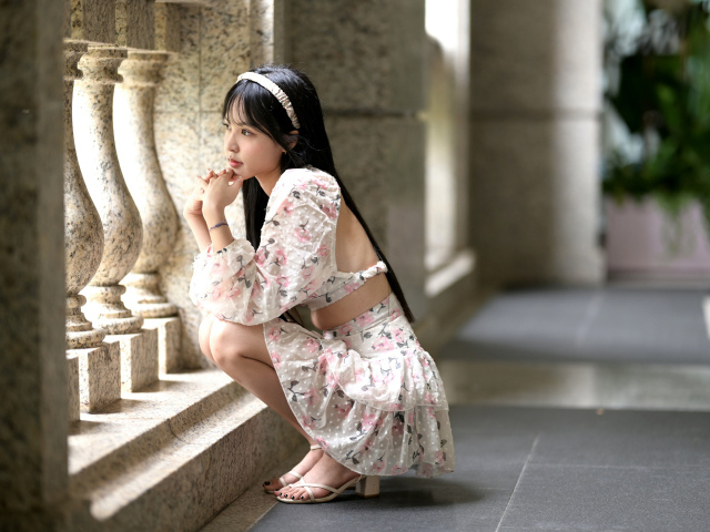 Красивая девушка азиатка в костюме сидит у стены