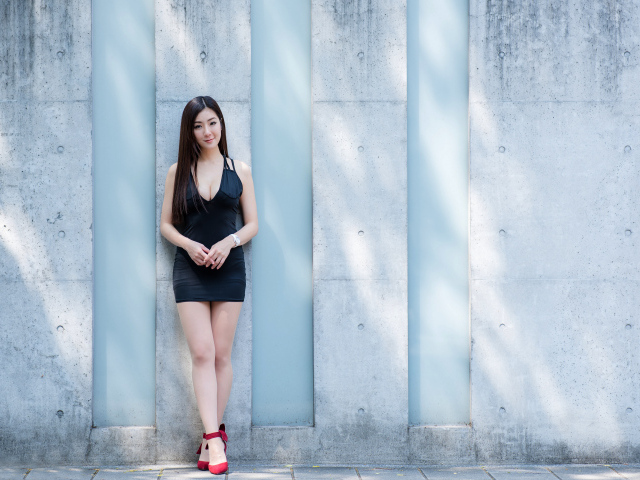 Красивая азиатка в коротком платье стоит у стены