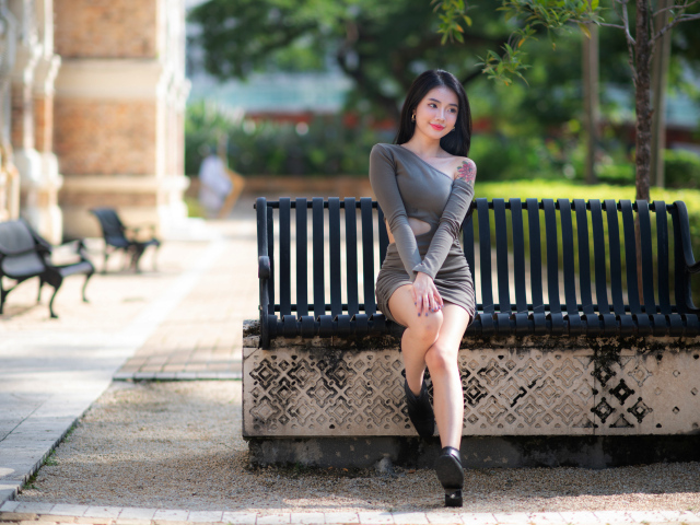 Милая азиатка в сером платье сидит на лавке