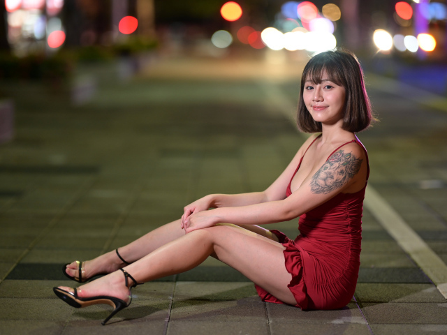 Милая азиатка в красном платье сидит на дороге