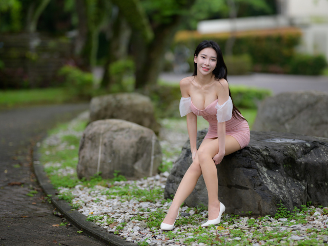 Милая азиатка в коротком платье сидит на камне
