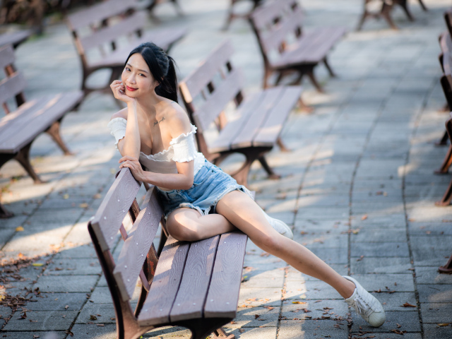 Милая девушка азиатка сидит на лавке в парке