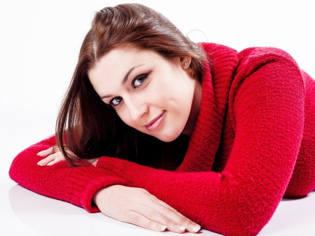 Милая брюнетка в красном свитере лежит на белом фоне