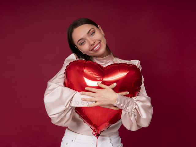 Улыбающаяся девушка обнимает шар в форме сердца