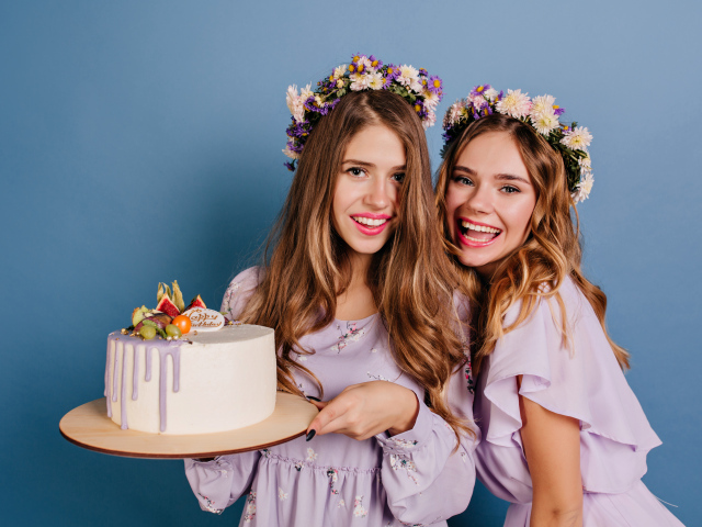 Две веселые молодые девушки с тортом на голубом фоне