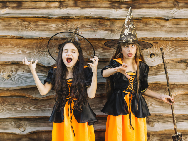 Две девочки в костюме ведьмы у стены на Хэллоуин