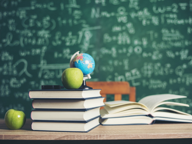 Книги на столе с зелеными яблоками и глобусом на фоне доски
