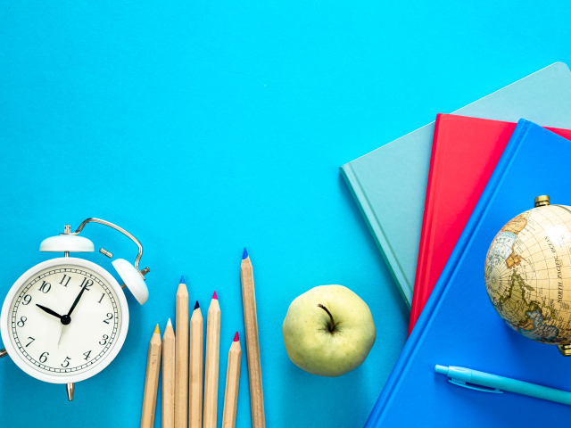 Книги на столе с глобусом, карандашами и будильником