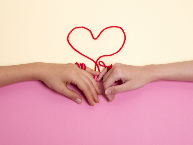 Человеческие руки связаны красной нитью в форме сердца