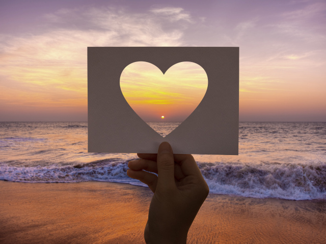 Бумажное сердце на фоне моря на закате солнца