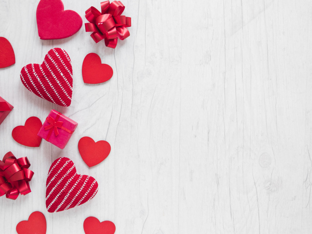 Красные сердечки с подарками и бантами на деревянном фоне