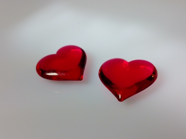 Два красных стеклянных сердца на сером фоне