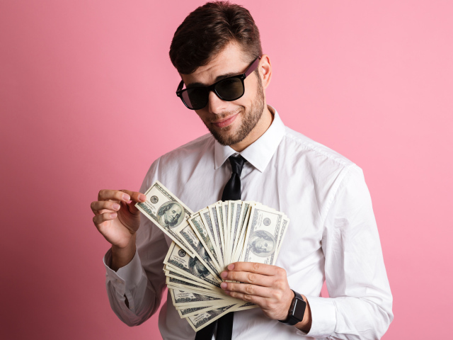 Деловой мужчина в черных очках с пачкой денег на розовом фоне