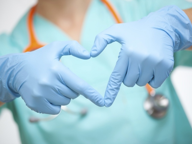 Доктор в медицинский перчатках делает сердце руками