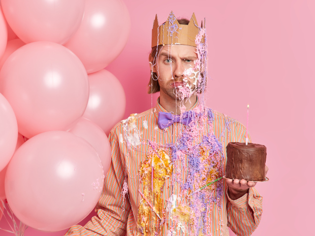 Мужчина принц с тортом и шариками на розовом фоне