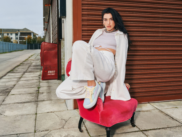 Певица Дуа Липа в белом костюме на кресле у стены