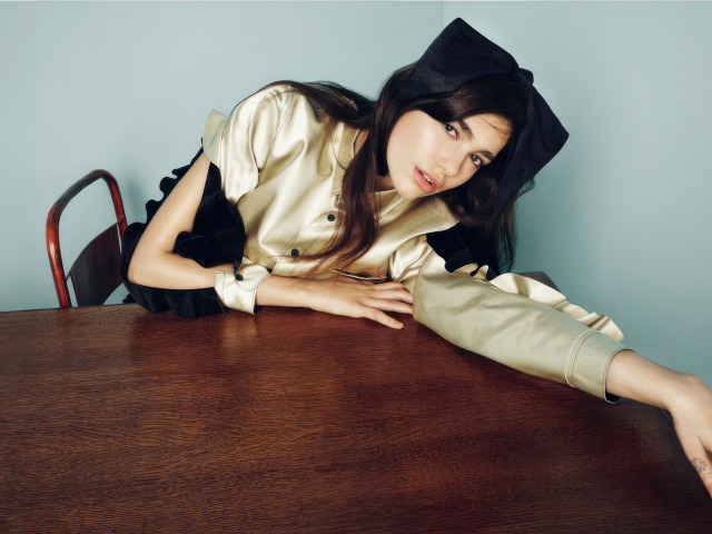 Певица Дуа Липа сидит за деревянным столом