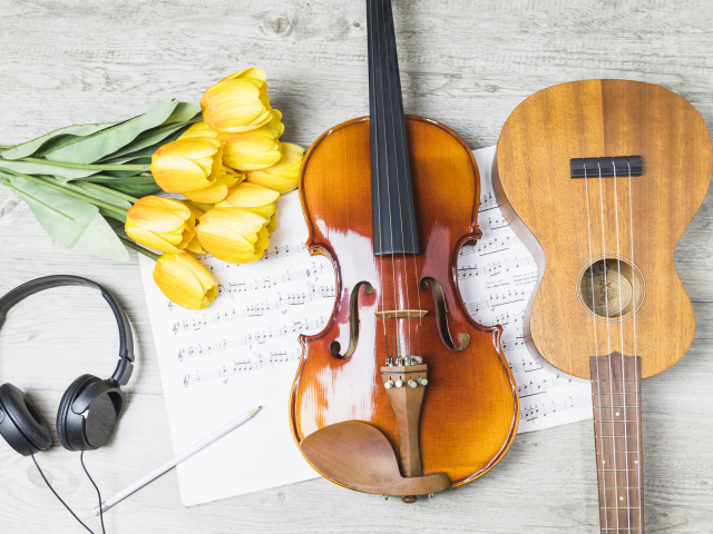 Маленькая гитара и скрипка на столе с нотами, наушниками и букетом тюльпанов