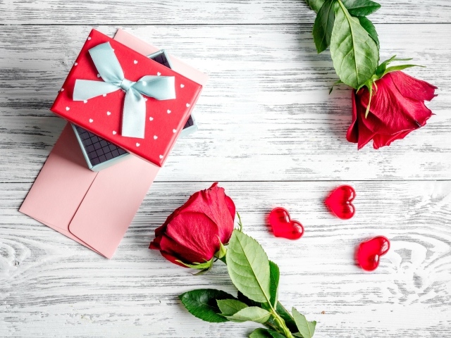 Две красные розы с подарком и сердечками на столе