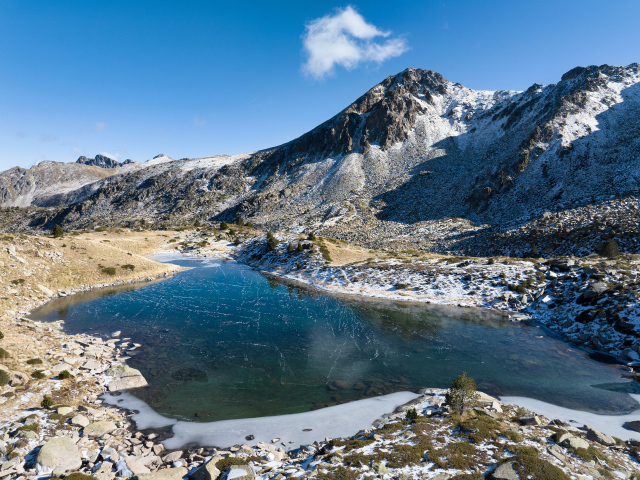 Покрытое льдом озеро в заснеженных горах в лучах солнца, Андорра