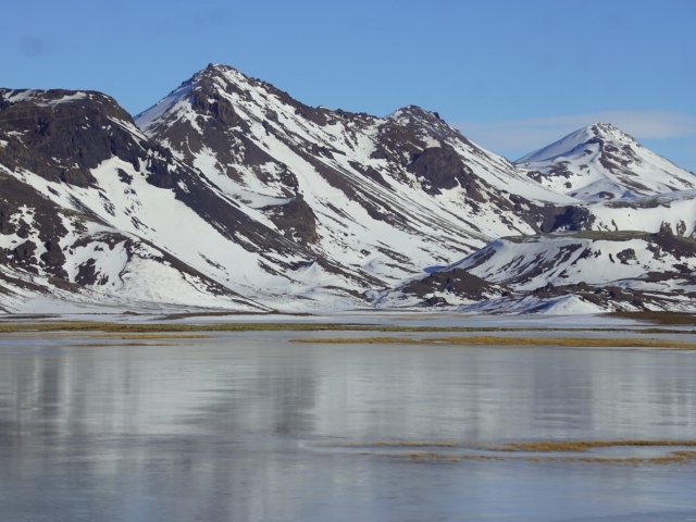 Горы в снегу под голубым небом у воды