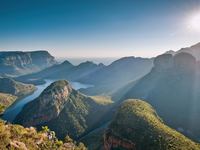 Яркое солнце над горами у реки летом