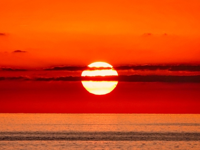 Яркое солнце в облаках на закате над морем 