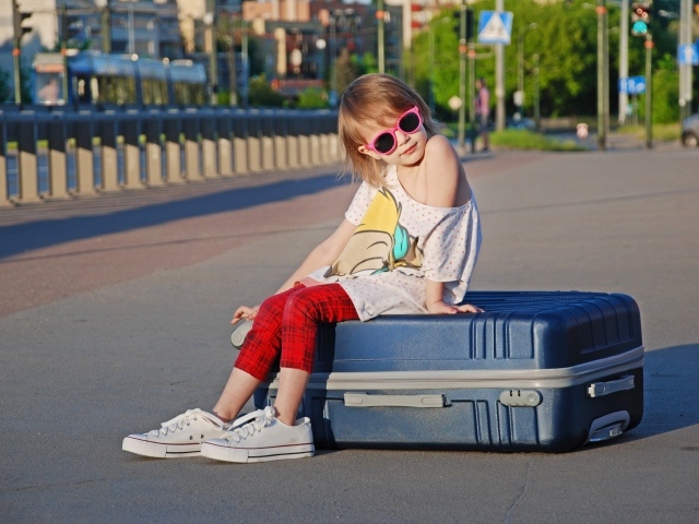 Девочка в солнечных очках сидит на чемодане на дороге