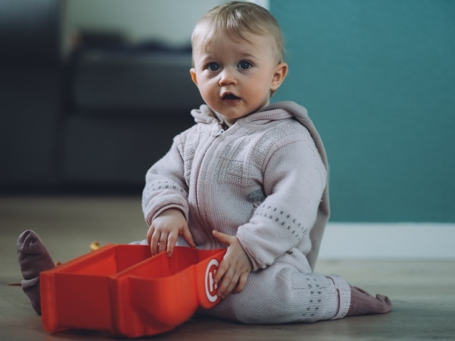 Маленький мальчик в теплом костюме сидит на полу