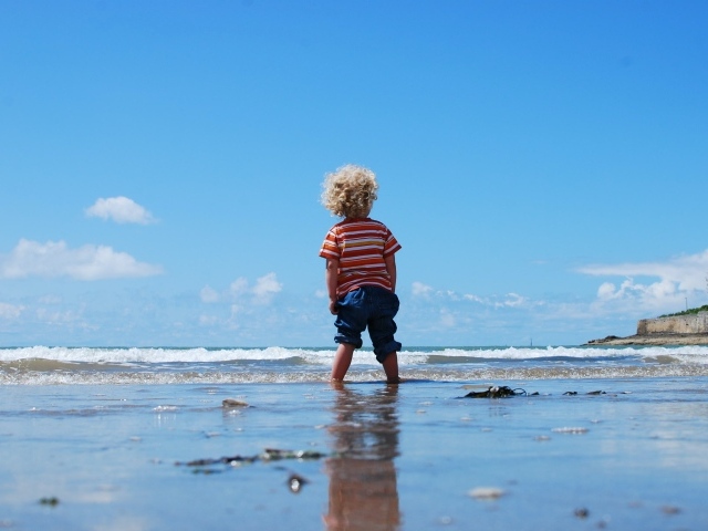 Маленький мальчик гуляет по мокрому песку у моря