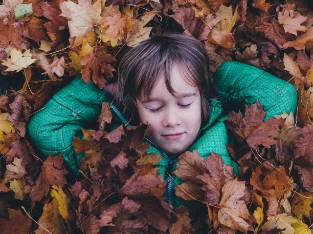 Маленькая девочка с закрытыми глазами лежит в сухой листве