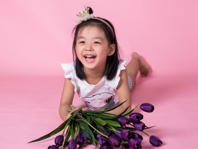 Девочка азиатка в букетом тюльпанов на розовом фоне