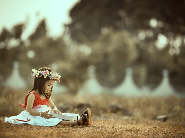 Девочка азиатка сидит с книгой на земле