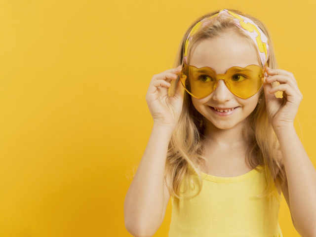 Красивая девочка блондинка в очках в форме сердца на желтом фоне