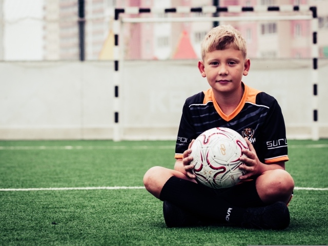 Мальчик футболист сидит на траве с мячом