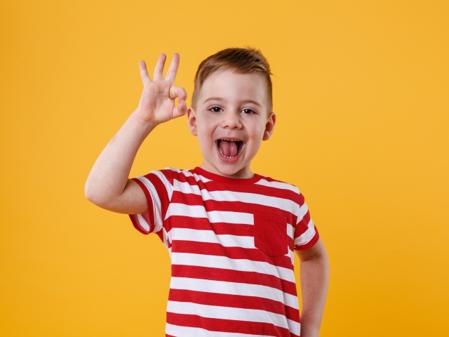 Веселый мальчик в полосатой футболке на оранжевом фоне