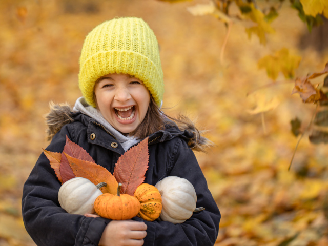 Веселая девочка с тыквами и листьями в руках осенью