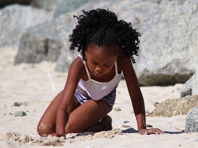 Темнокожая маленькая девочка играет на песке на пляже