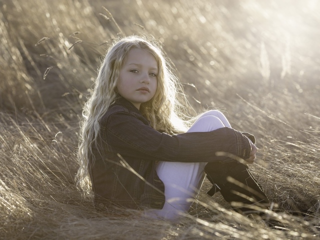 Маленькая светловолосая девочка сидит на сене